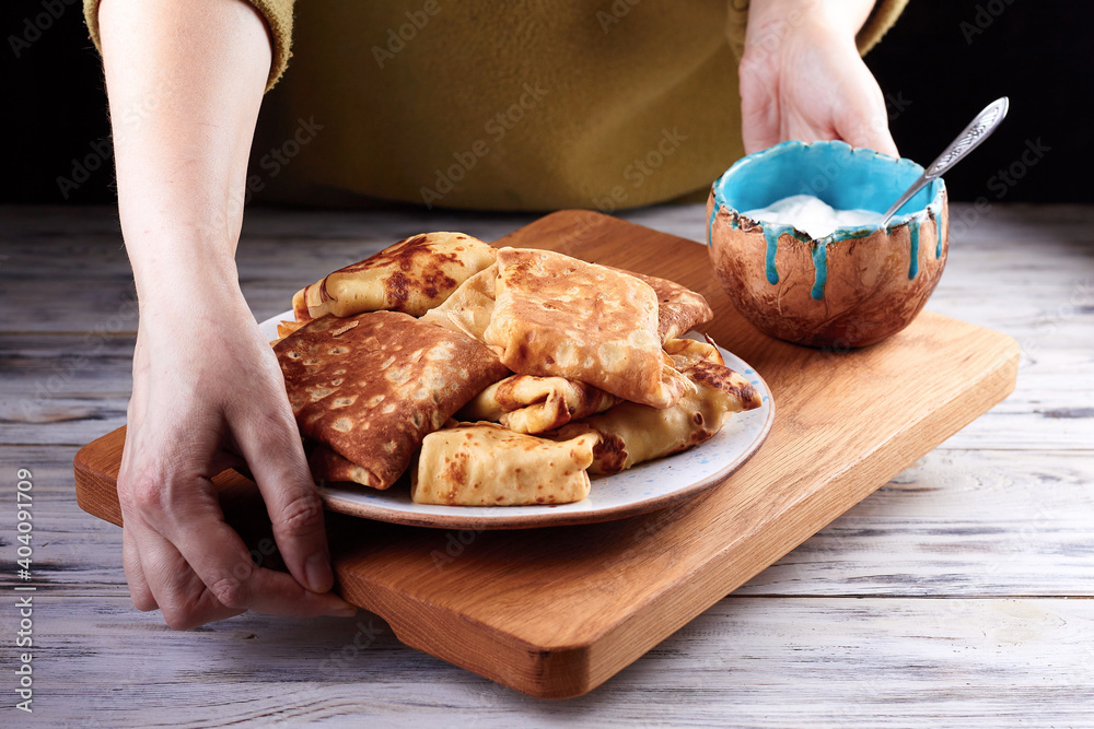 Homemade crepes, tasty thin pancakes on plate with a bowl of sour cream on old wooden plank in female hands Homemade crepes, tasty thin pancakes on plate with a bowl of sour cream on old wooden plank in female hands