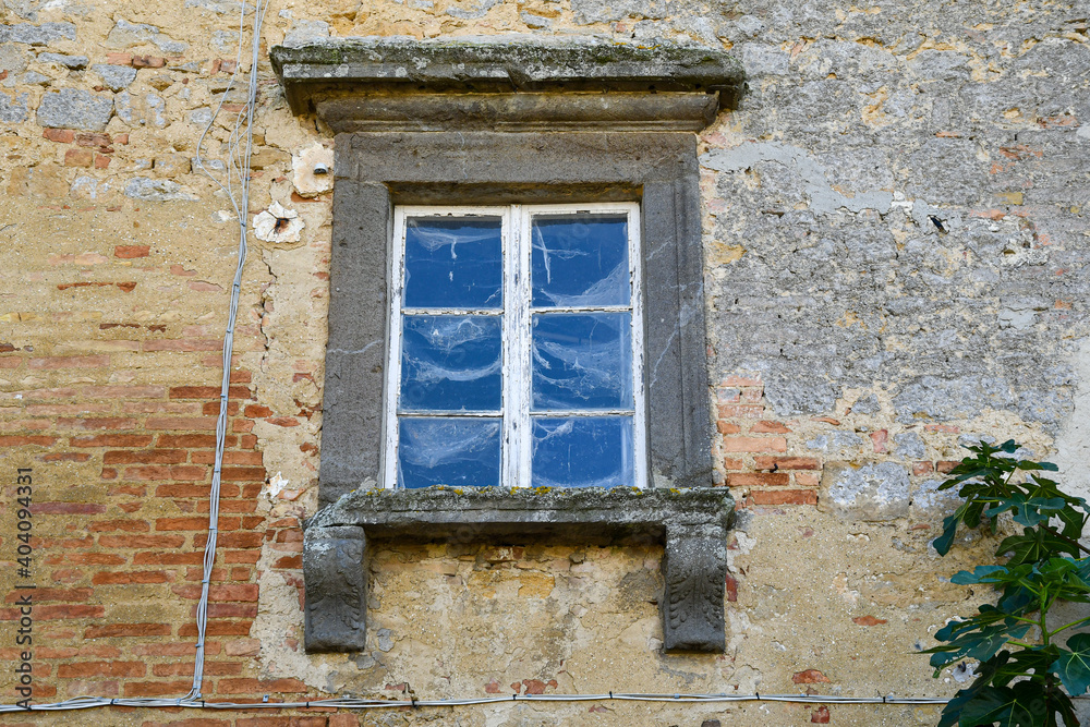 The stone framed window of an old stone and brick house with a branch of a fig tree, Volterra, Pisa, Tuscany, Italy The stone framed window of an old stone and brick house with a branch of a fig tree, Volterra, Pisa, Tuscany, Italy