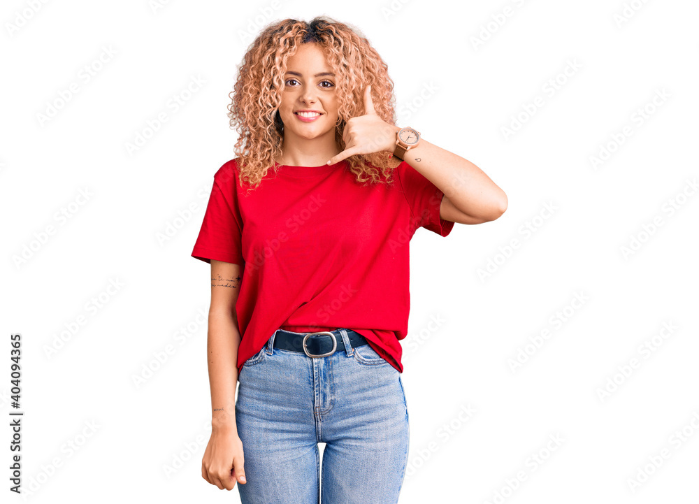 Young blonde woman with curly hair wearing casual red tshirt smiling doing phone gesture with hand and fingers like talking on the telephone. communicating concepts. Young blonde woman with curly hair wearing casual red tshirt smiling doing phone gesture with hand and fingers like talking on the telephone. communicating concepts.