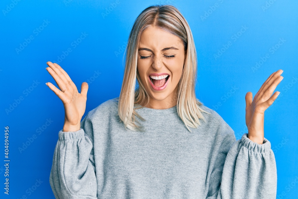 Beautiful blonde woman wearing casual clothes celebrating mad and crazy for success with arms raised and closed eyes screaming excited. winner concept Beautiful blonde woman wearing casual clothes celebrating mad and crazy for success with arms raised and closed eyes screaming excited. winner concept