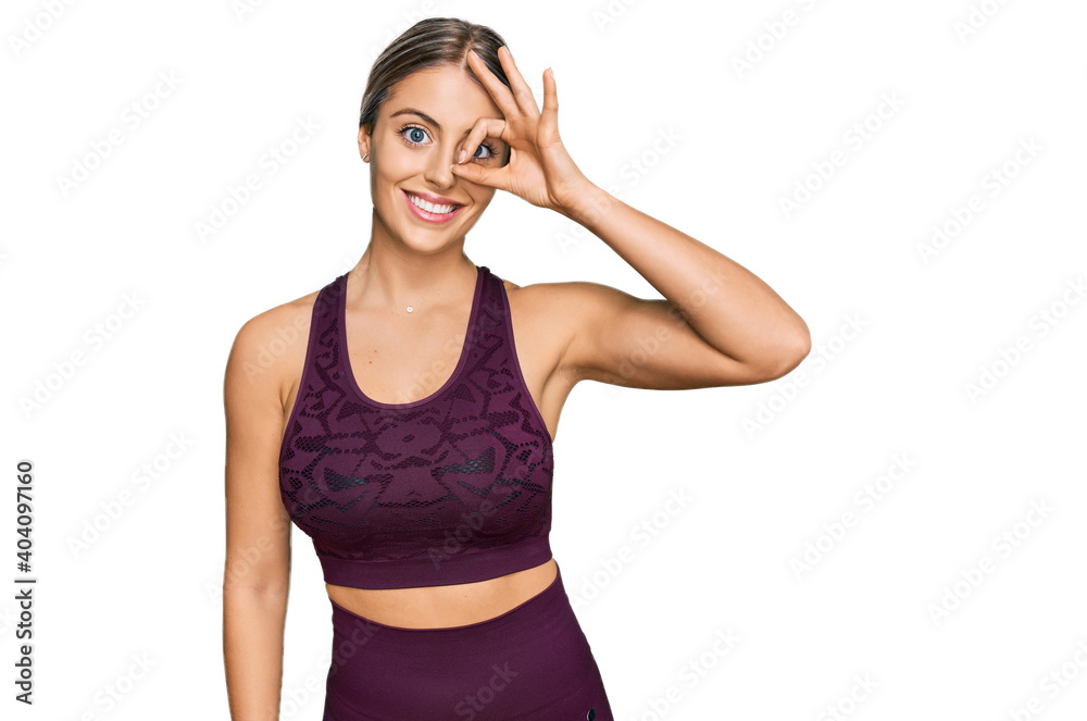 Beautiful blonde woman wearing sportswear smiling happy doing ok sign with hand on eye looking through fingers Beautiful blonde woman wearing sportswear smiling happy doing ok sign with hand on eye looking through fingers