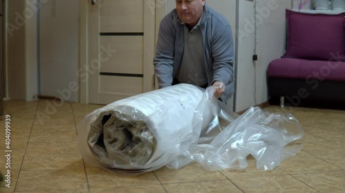 A grown man unpacks a new mattress. Unpacking the mattress with a knife pressed into the bag