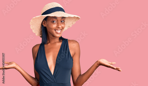 Young african american woman wearing swimsuit and summer hat smiling showing both hands open palms, presenting and advertising comparison and balance