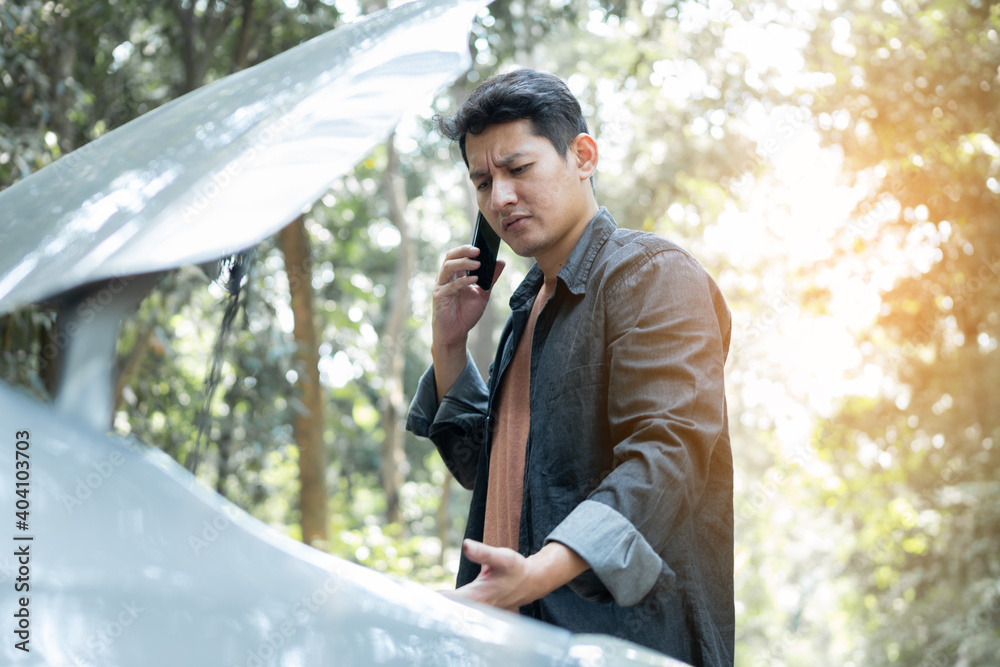 Man using phone for contact maintenance car service. Man trying to repair a car engine, looking inside open bonnet Man using phone for contact maintenance car service. Man trying to repair a car engine, looking inside open bonnet