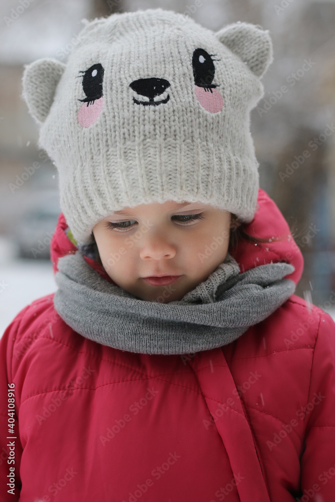 Little girl in the street in winter in a funny hat and red jacket Little girl in the street in winter in a funny hat and red jacket