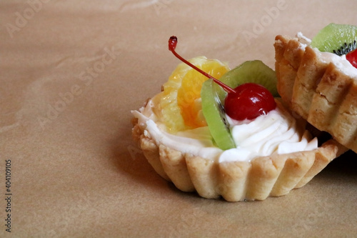 Fruit basket cake filled with whipped cream or cream, orange and kiwi wedges and garnished with cherries in sugar syrup