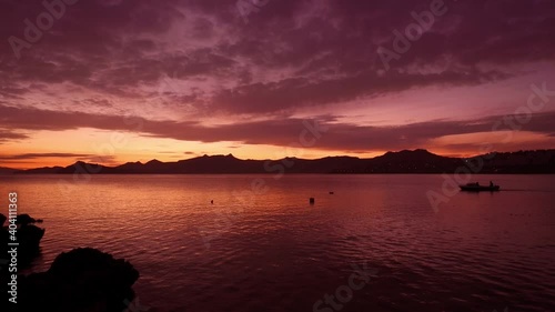 Cinematic golden hour sunset over Aegean Sea with silhouette of Bodrum peninsula mountains, calm reflecting water and small fishing boat, Mugla Turkey
