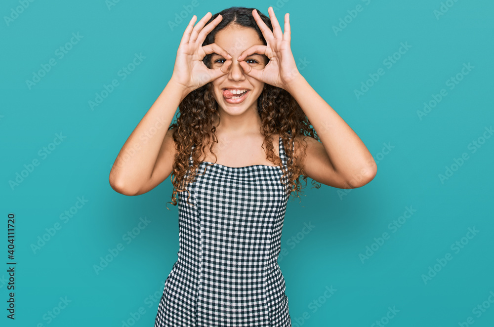 Teenager hispanic girl wearing casual clothes doing ok gesture like binoculars sticking tongue out, eyes looking through fingers. crazy expression. Teenager hispanic girl wearing casual clothes doing ok gesture like binoculars sticking tongue out, eyes looking through fingers. crazy expression.
