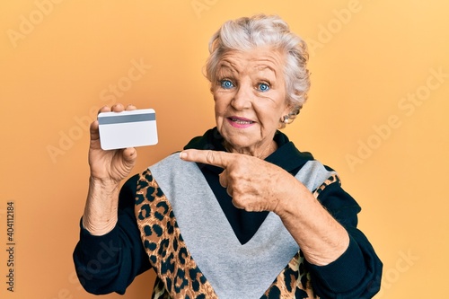 Senior grey-haired woman holding credit card smiling happy pointing with hand and finger