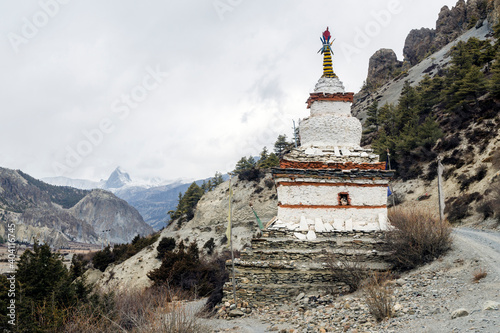 Buddhist white stupa and snow capped mountain peak near Braga on the Annapurna Circuit trail, Nepal