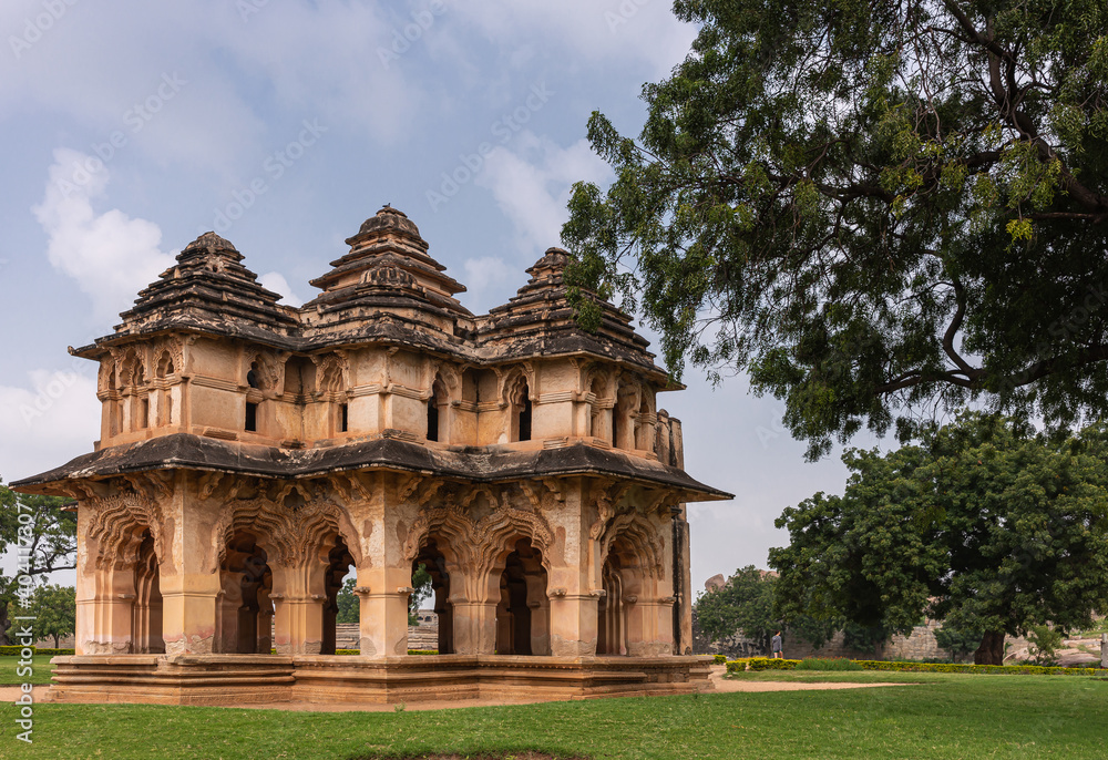 Hampi, Karnataka, India - November 5, 2013: Zanana Enclosure. Brown stone ruinous Lotus Mahal building in green park under blue cloudscape. Green foliage on side.