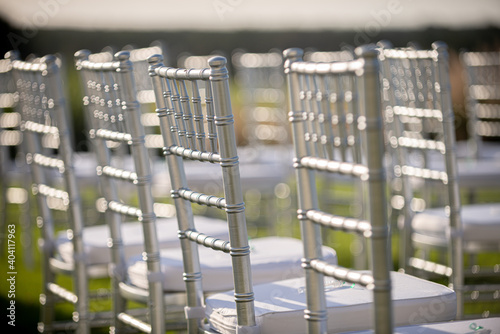Silver chiavari chairs with white cushions at outdoor wedding ceremony  with white bokeh background