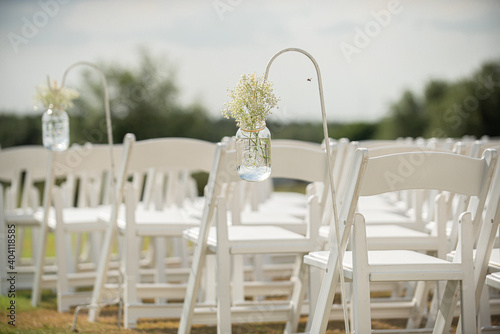 Fancy white folding chairs lined  up at outdoor wedding ceremony with babyie's breathe flowers in mason jars hanging