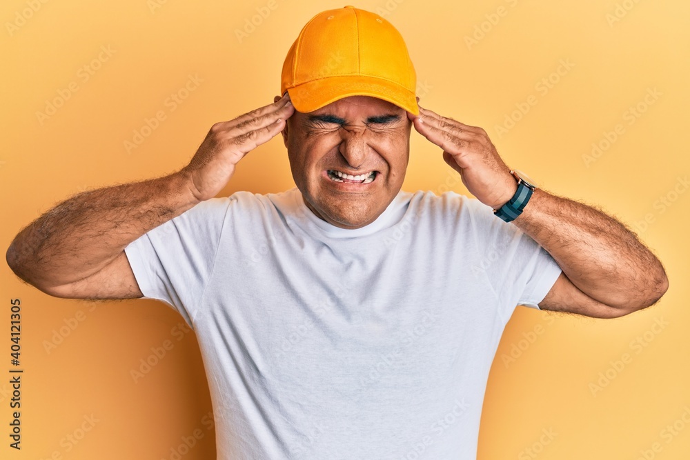 Mature middle east man with mustache wearing casual white tshirt and yellow cap with hand on head, headache because stress. suffering migraine.