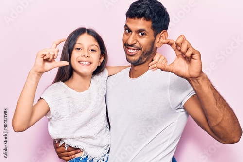 Young father and daughter wearing casual clothes smiling and confident gesturing with hand doing small size sign with fingers looking and the camera. measure concept.