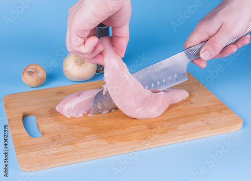 cutting chicken breast on a wooden board with a cutting, steel knife