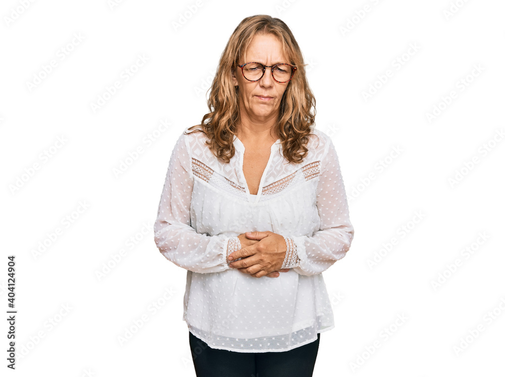 Middle age blonde woman wearing casual white shirt and glasses with hand on stomach because indigestion, painful illness feeling unwell. ache concept. Middle age blonde woman wearing casual white shirt and glasses with hand on stomach because indigestion, painful illness feeling unwell. ache concept.