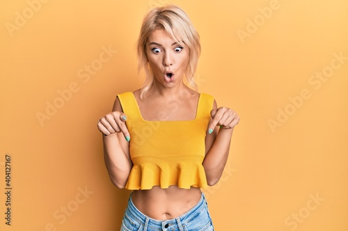 Young blonde girl wearing casual clothes pointing down with fingers showing advertisement, surprised face and open mouth © Krakenimages.com