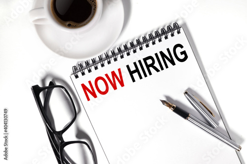 NOW HIRING, text on white paper, ON NOTEBOOK, light and white background