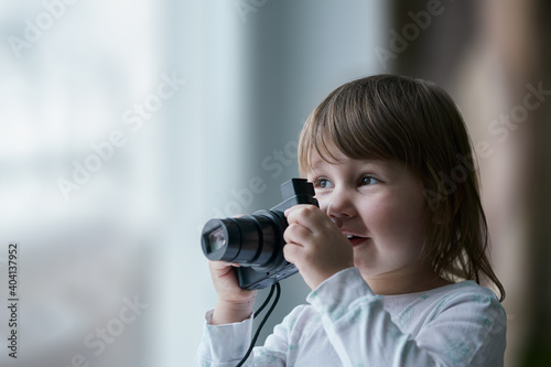 Happy little girl sitting with a camera at the window. Selective focus.. Copy space.