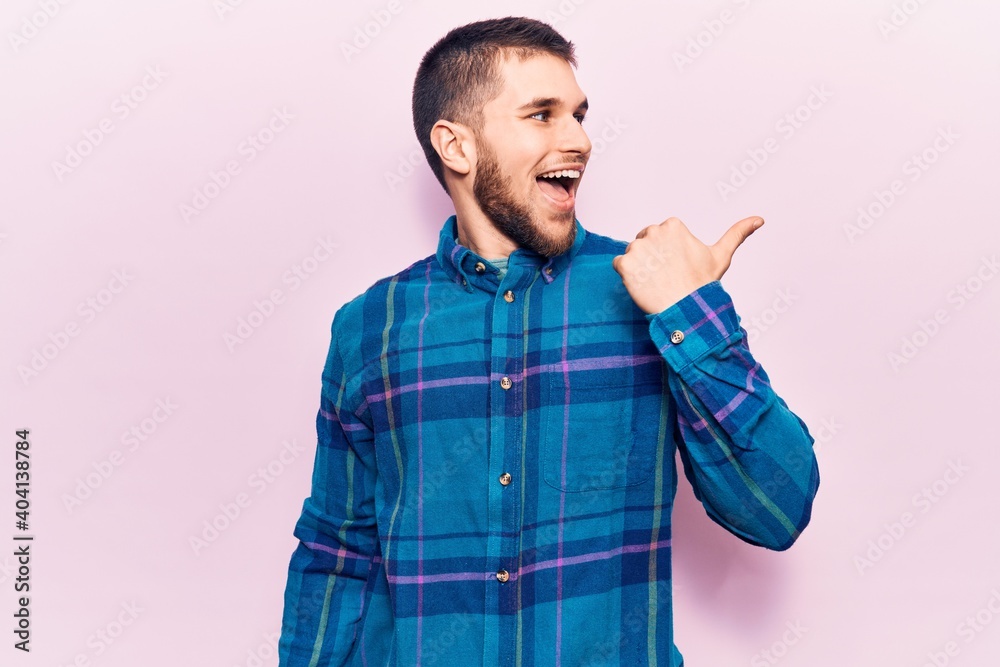 Young handsome man wearing casual shirt pointing thumb up to the side smiling happy with open mouth Young handsome man wearing casual shirt pointing thumb up to the side smiling happy with open mouth
