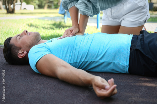 Young woman performing CPR on unconscious man outdoors. First aid