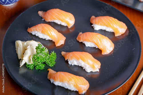 Salmon sushi typical of Japanese cuisine on black plate, natural light inside restaurant