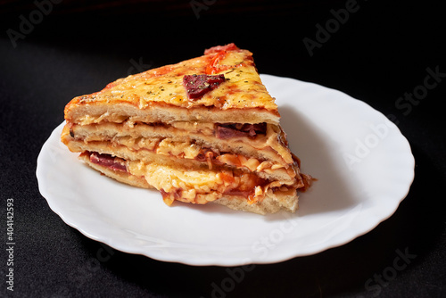 A piece of Italian Pizza Cake with four layers full of grilled salami, ham and moose sausage. Black background.