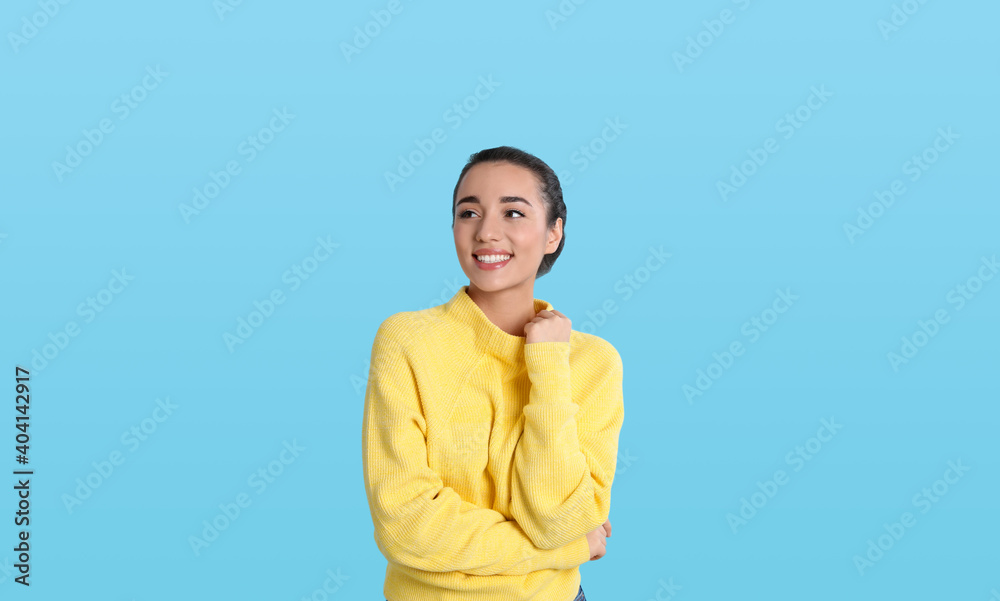 Beautiful young woman wearing yellow warm sweater on light blue background Beautiful young woman wearing yellow warm sweater on light blue background