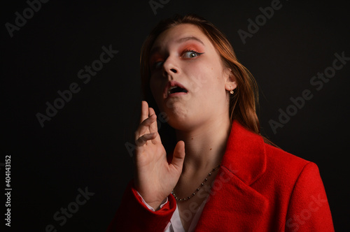 Close-up of a young girl in a red coat with a raised palm up against a dark background. A dramatic photo with a vivid emotion of disgust, fear, surprise.