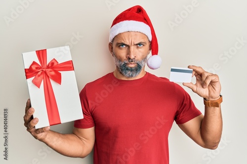 Middle age handsome man wearing chrismast hat holding gift and credit card skeptic and nervous, frowning upset because of problem. negative person. photo