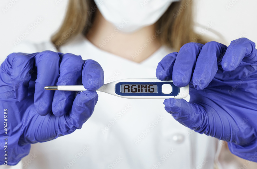 The doctor holds a thermometer in his hands, on the electronic screen of which it is written - AGING The doctor holds a thermometer in his hands, on the electronic screen of which it is written - AGING