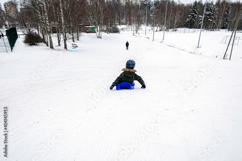 The child is sledding down the hill. Downhill skiing in winter.