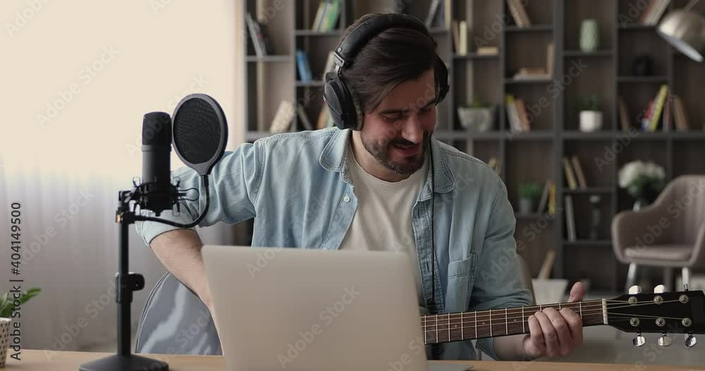 Young man sit indoor greeting learner start videoconference call on laptop play acoustic guitar, on-line teacher wear headphones teaches remotely play string instrument. Online tutoring, hobby concept Young man sit indoor greeting learner start videoconference call on laptop play acoustic guitar, on-line teacher wear headphones teaches remotely play string instrument. Online tutoring, hobby concept
