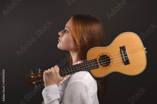 Girl with ukulele in profile on a black background..Music of romantic mood, online ukulele training..