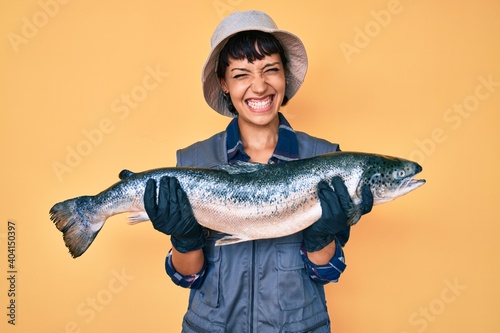 Beautiful brunettte fisher woman showing raw salmon smiling and laughing hard out loud because funny crazy joke. photo