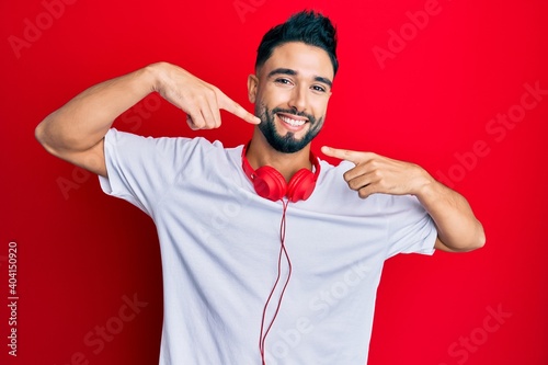 Young man with beard listening to music using headphones smiling cheerful showing and pointing with fingers teeth and mouth. dental health concept.