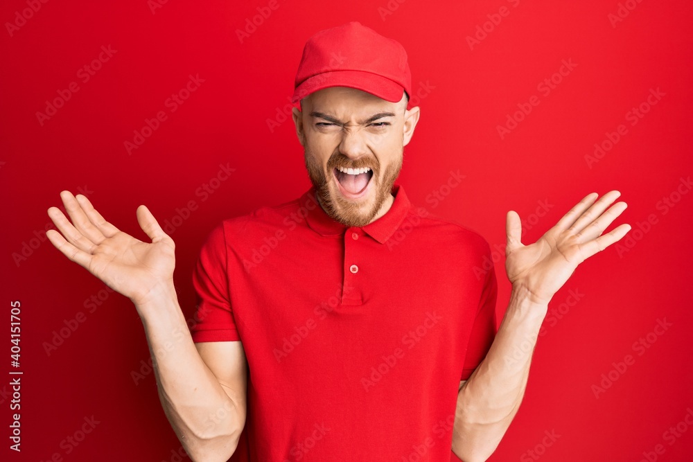 Young redhead man wearing delivery uniform and cap celebrating mad and crazy for success with arms raised and closed eyes screaming excited. winner concept Young redhead man wearing delivery uniform and cap celebrating mad and crazy for success with arms raised and closed eyes screaming excited. winner concept