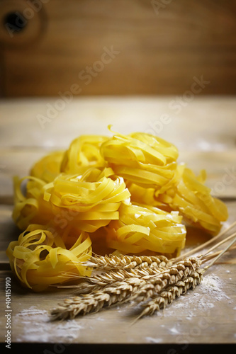 Selective focus. Fettuccine pasta on a wooden surface. Flour and ears of wheat. The concept of making pasta from durum wheat.