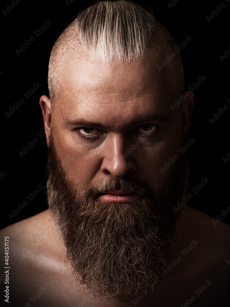 Handsome brutal caucasian bearded man in the dark. Studio portrait. Low key. Closeup. Vertical orientation.