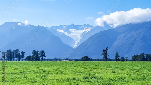 Stunning view of Fox Glacier on the west coast of New Zealand on a clear and sunny day. The area lies next to the southern alps and is surrounded by mountains and  green farm land.  photo