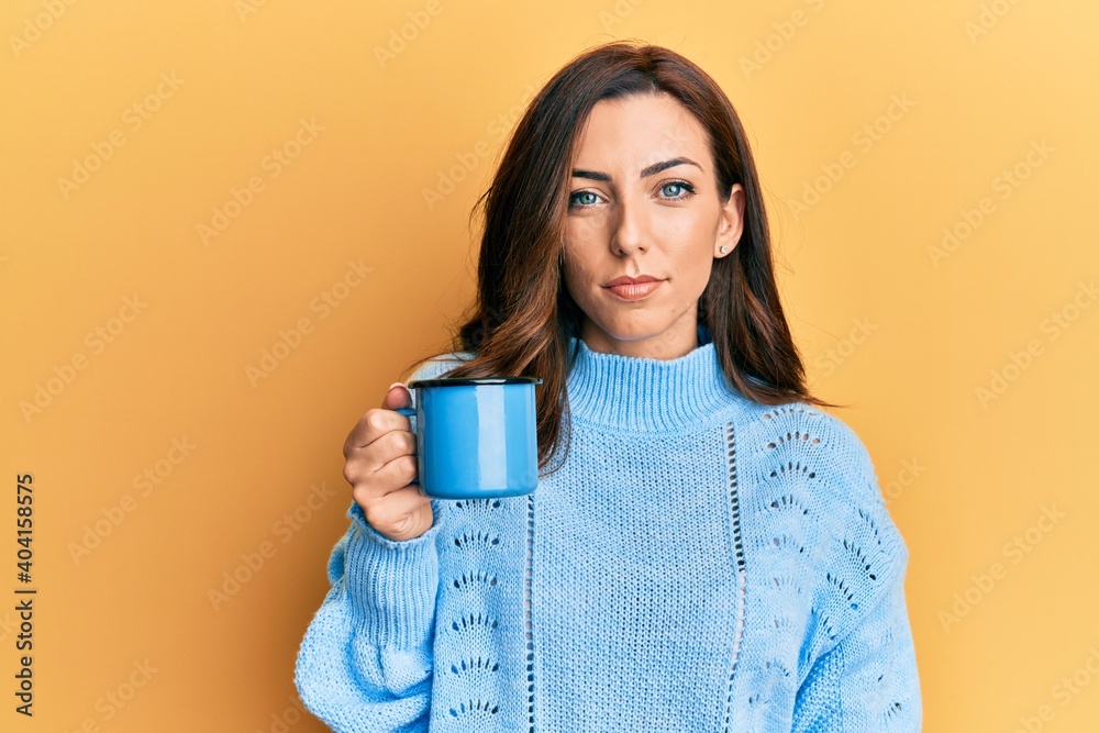 Young brunette woman holding a cup of coffee thinking attitude and sober expression looking self confident Young brunette woman holding a cup of coffee thinking attitude and sober expression looking self confident