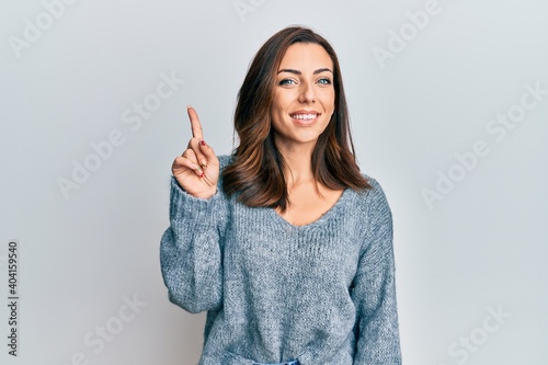 Young brunette woman wearing casual winter sweater showing and pointing up with finger number one while smiling confident and happy.