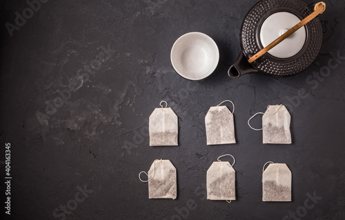 Tea bags with tea pot and cup on black stone background