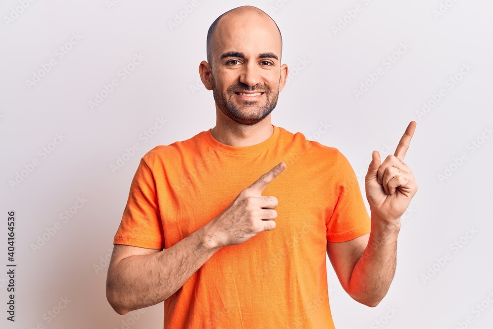 Fototapeta premium Young handsome bald man wearing casual t shirt smiling and looking at the camera pointing with two hands and fingers to the side.
