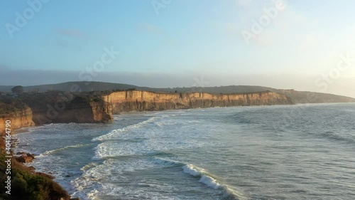 AERIAL LIFT Powerful Waves Roll Into Limestone Cliffs During Golden Hour photo