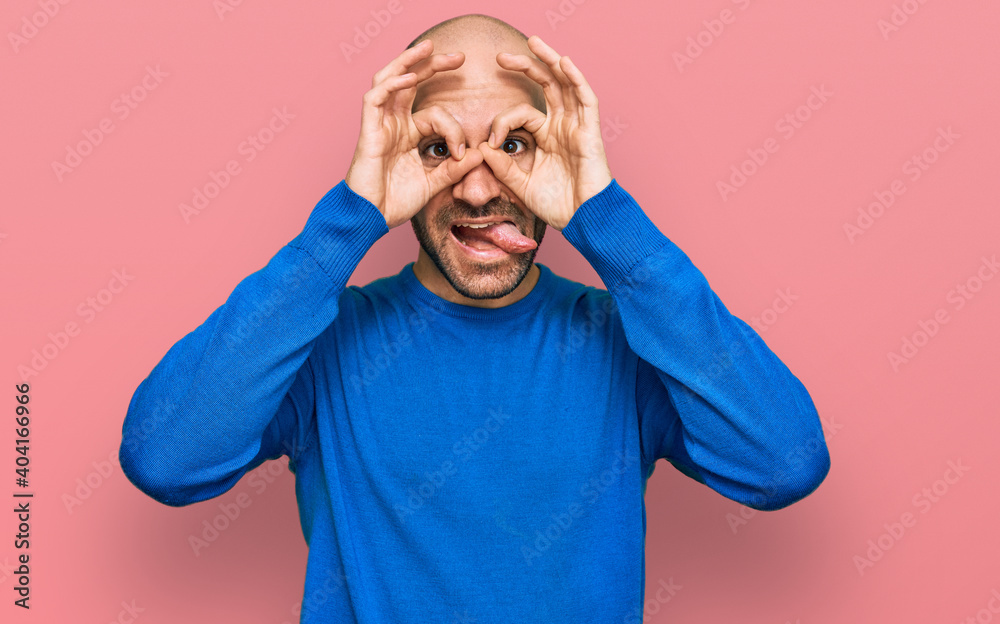 Young hispanic man wearing casual clothes doing ok gesture like binoculars sticking tongue out, eyes looking through fingers. crazy expression.