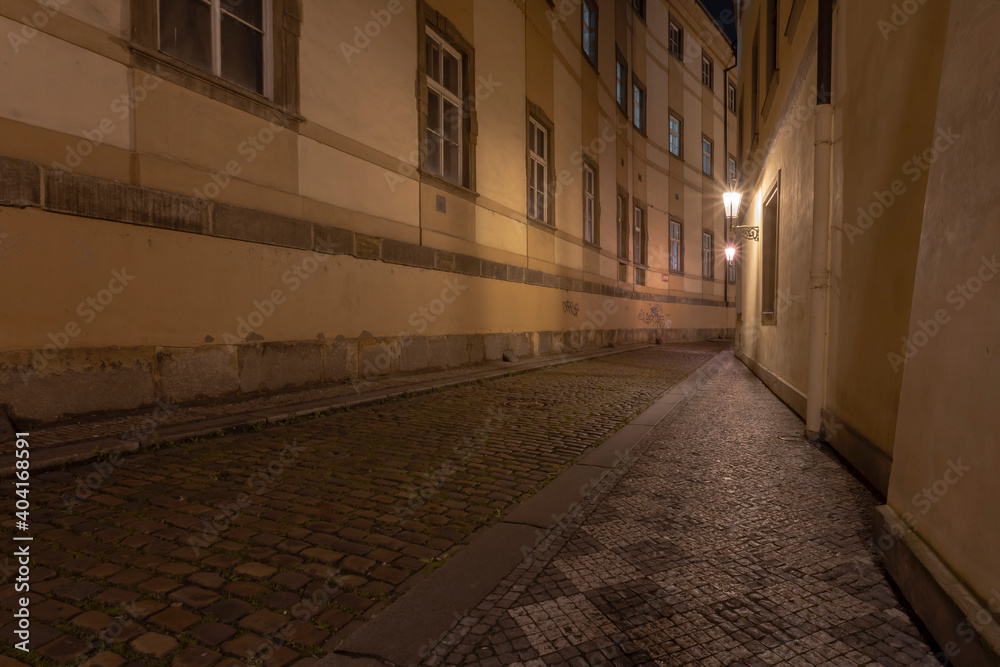 .lit street lights and a cobbled street with cobblestones in the center of Prague at night