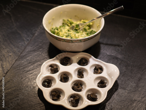 One dozen of snails on white plate with snail butter preparation. Perspective view.