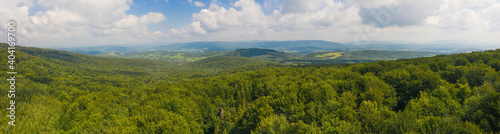 Fototapeta Naklejka Na Ścianę i Meble -  Vast summer scenery with green forested hills from aerial perspective. Wide panoramic composition of untouched nature sunlit in the morning. Blue sky with clouds above landscape.